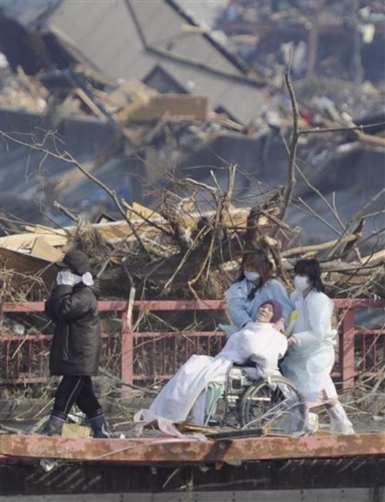 A patient in a wheelchair is helped by attendants as they evacuate from a tsunami-affected hospital at Otsuchi, northeastern Japan, on Sunday March 13, 2011, two days after a powerful earthquake and tsunami hit the the country's northeastern coast.